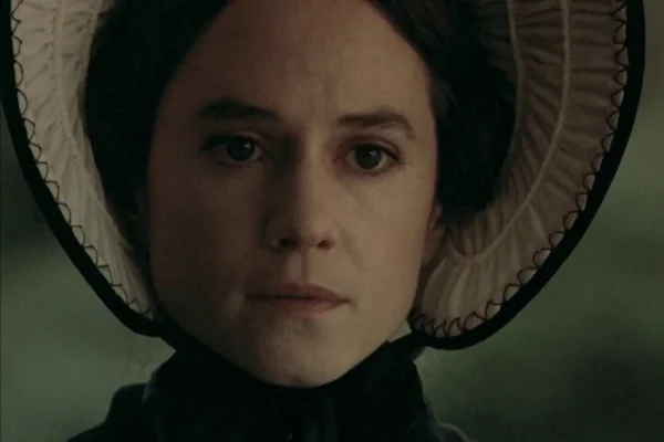 Close-up of a woman wearing a Victorian-style bonnet, looking somberly ahead.
